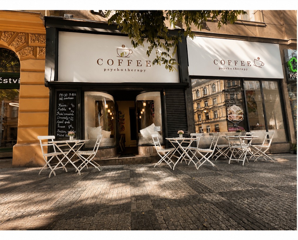 Kavárna Coffee Psycho Therapy na Francouzské ulici v Praze na Vinohradech — černý štít s krémovým vývěsním štítem a bílé stolky na chodníku